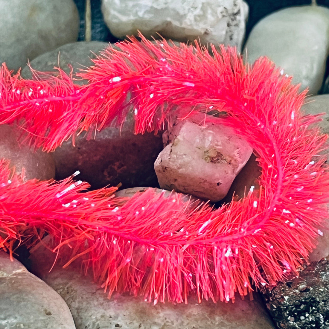 New Watermelon 15mm Fritz Hank coiled on river stones, showing vibrant pink-red colour with UV sparkle fibres